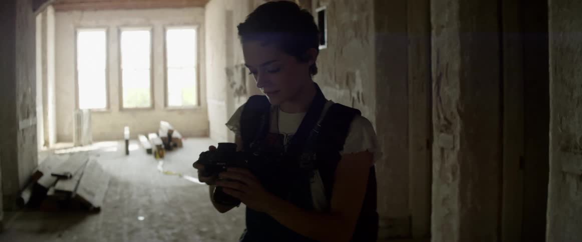 A white woman walks through the hallway of a decaying building while taking pictures