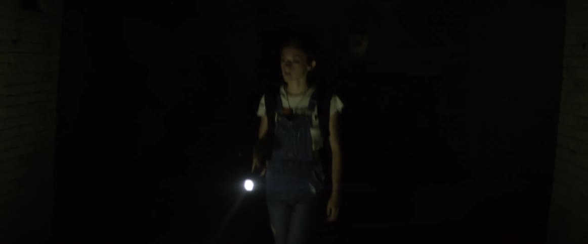 Short haired woman shines the flashlight into the dark room and notices someone behind her and gets scared then runs away