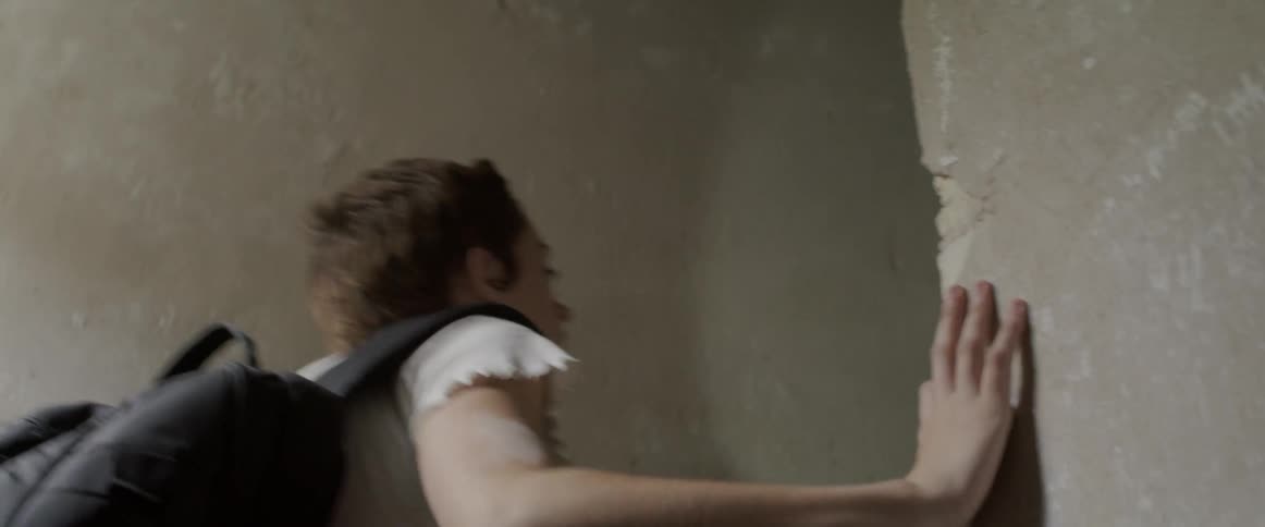 A woman with a backpack and a flashlight walking upstairs while touching the wall