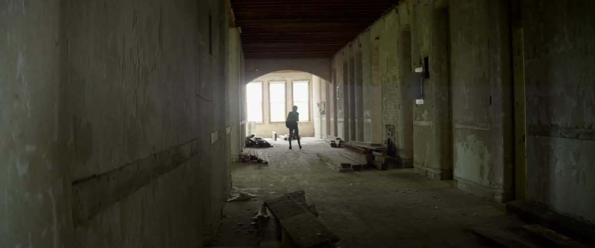 A photographer walks around a concrete building with stacks of lumber on the floor