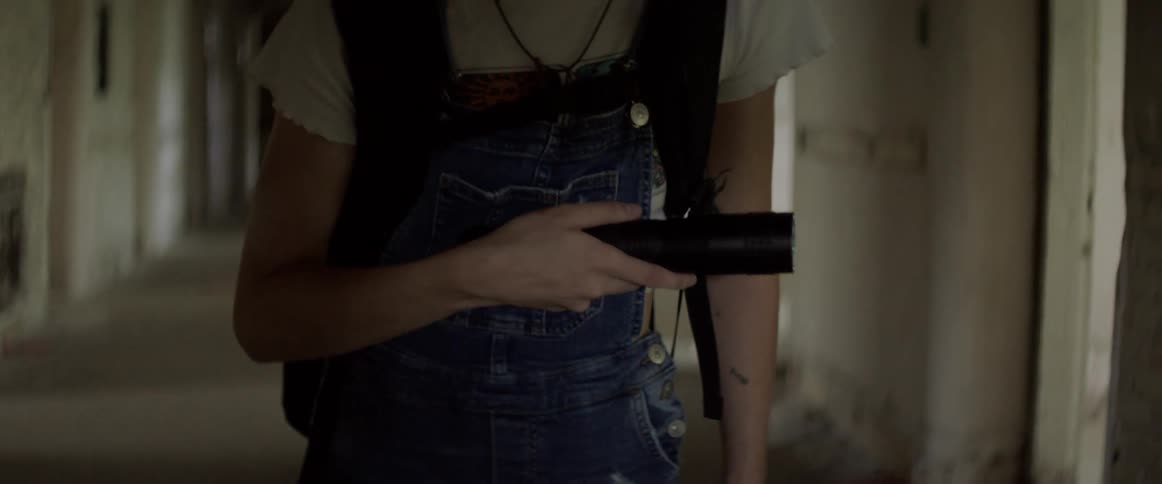 A white woman with a flashlight explores a hallway