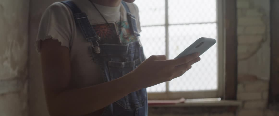 A woman in denim overalls takes a photo with a smartphone indoors