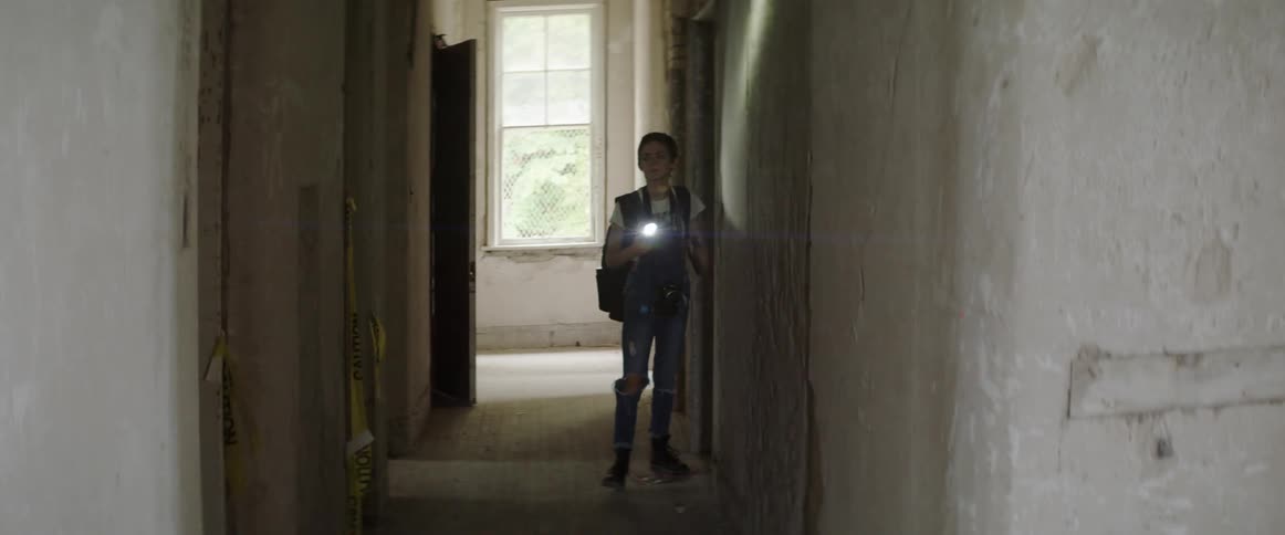 A woman shines a flashlight while looking around an empty hallway
