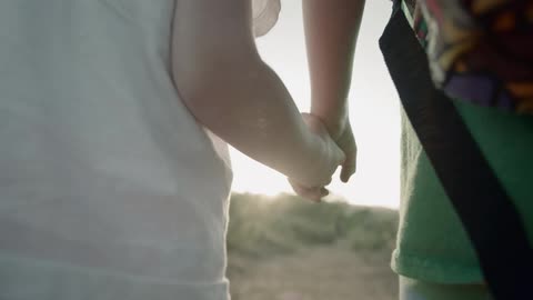 Siblings hold hands as they walk on a dirt trail on a sunny day