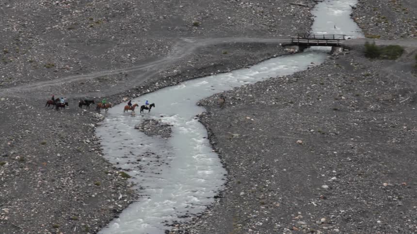 A line of people on horses cross a river
