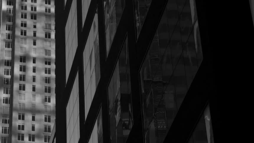 The glass faces of a city building reflects the surrounding buildings and sky