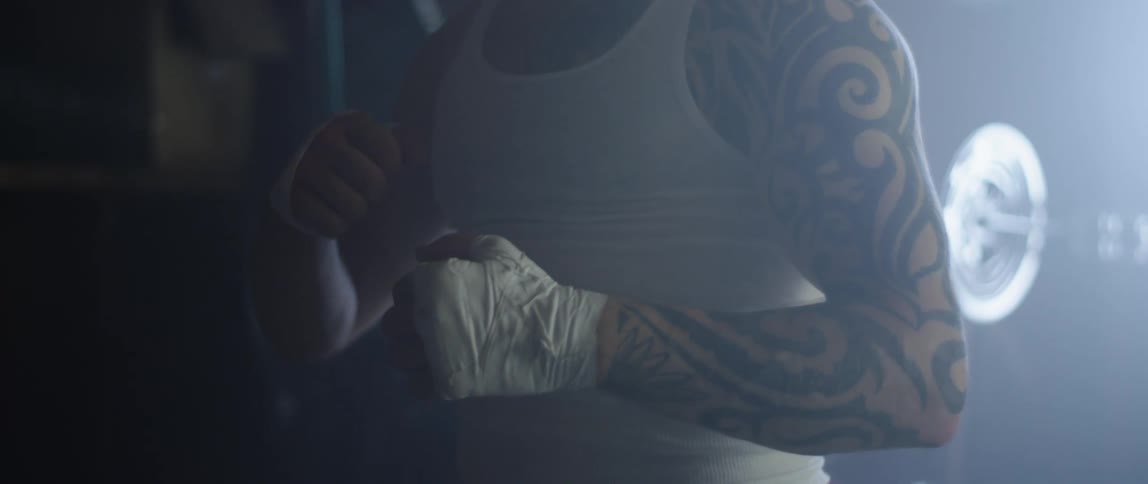 A tattooed man wearing boxing hand wraps punching his palms