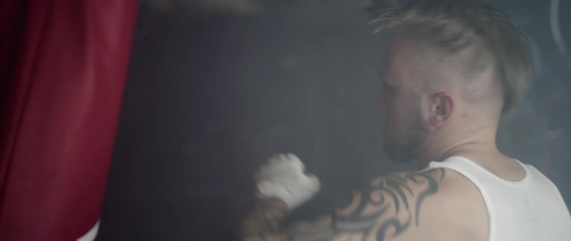 A white male boxer hits a punching bag in a gym
