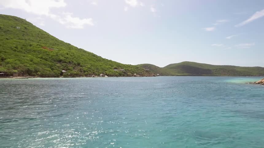 Light blue water off the coast of a hilly landmass during the day