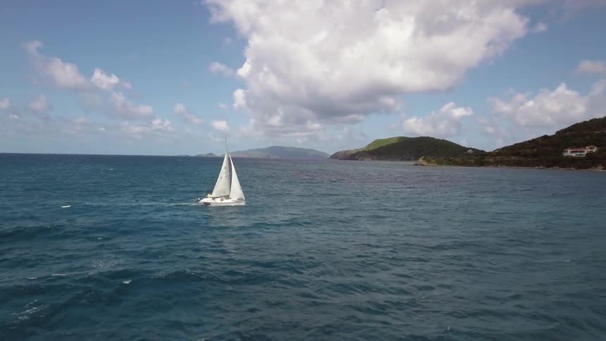 A sailboat traveling the ocean just off a hilly coast