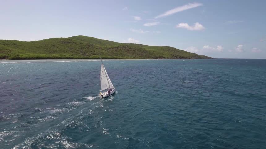 A person on a sailboat in the ocean with land and the sky in the background