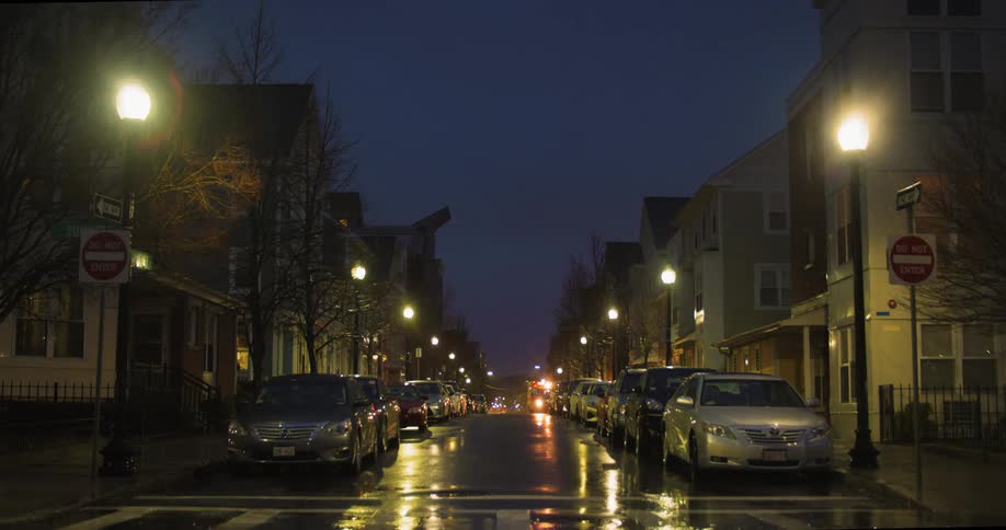 An ambulance sits on a neighborhood street crowded with parked vehicles