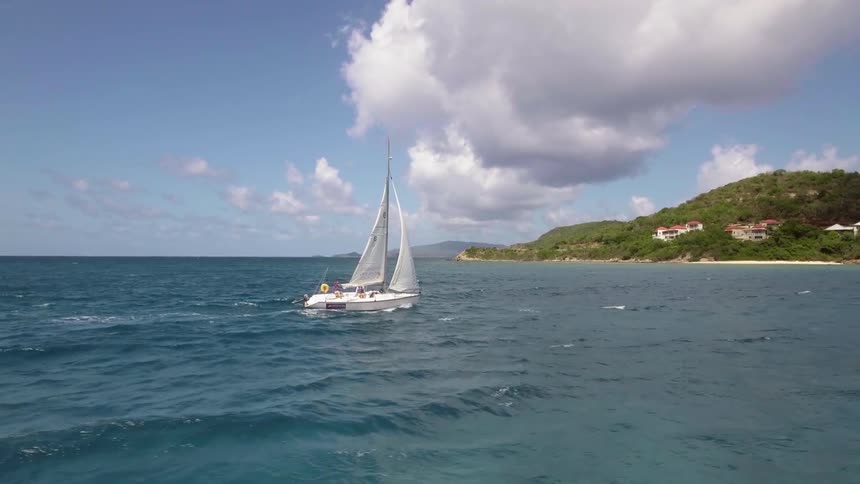 A sailboat on the ocean near the coast with the sky in the background