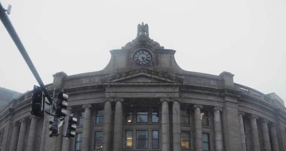 Its snowing in a downtown city and a building is displayed