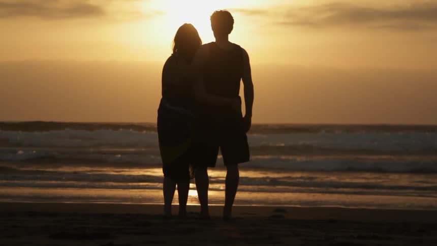 A man and woman kiss on the beach as the sun sets