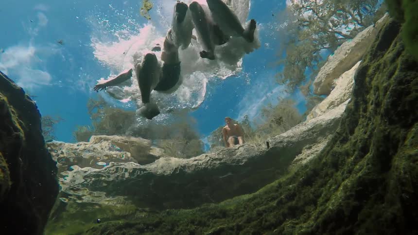 Two people jump into a clear pond