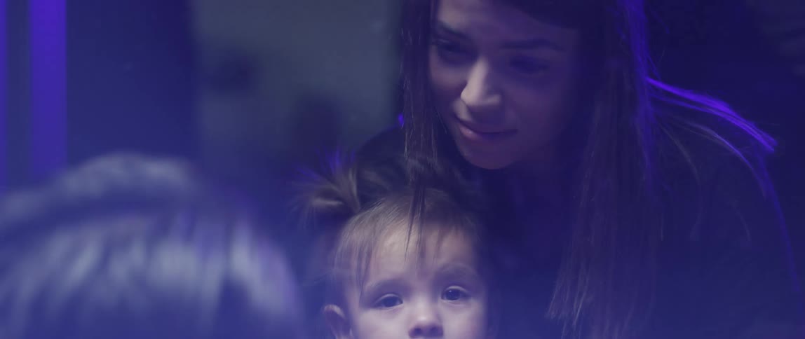 A child playing with clay while sitting the lap of a woman in a dimly lit room