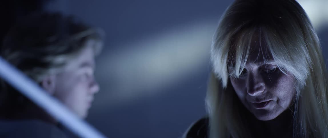 A blonde woman talks to her son and holds up a photograph