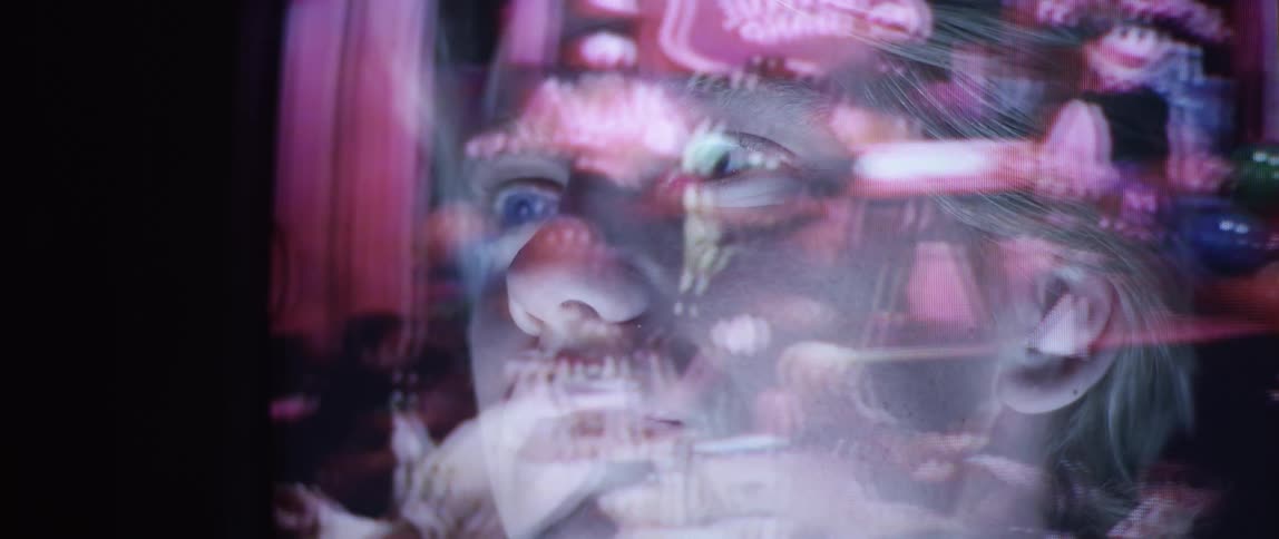 The images of a home movie are reflected across a mans face in the glass
