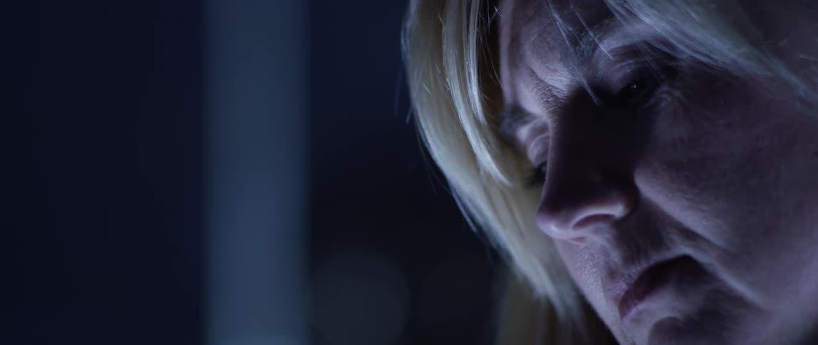 A middle aged woman in a dark room turning her head to look at something out of frame