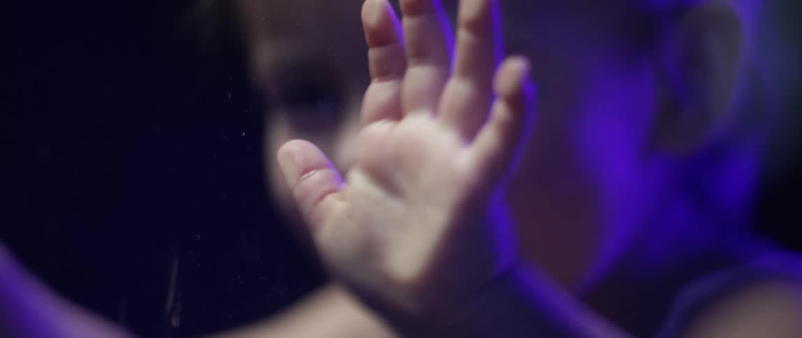 A little girl playing with a window in a room with colored light