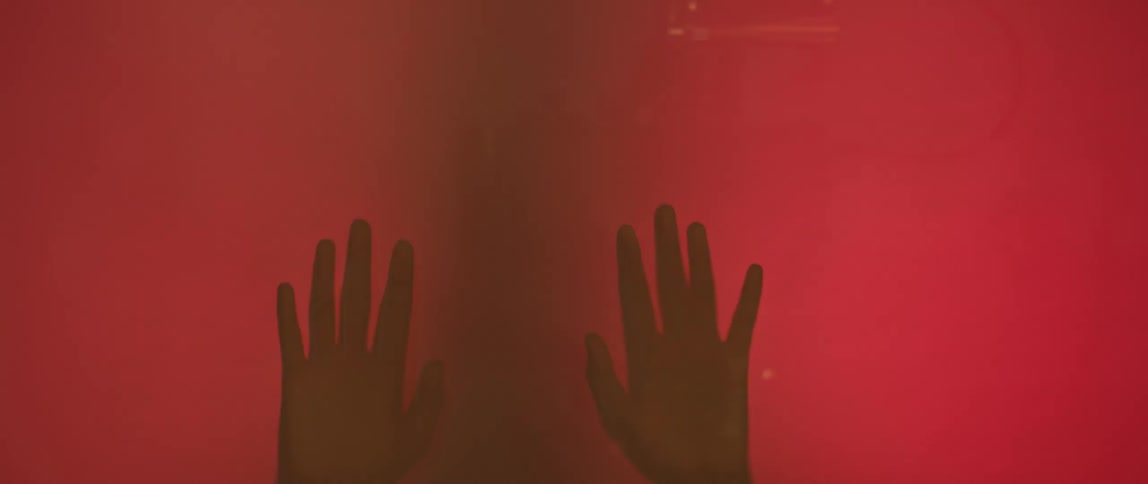 A pair of hands touch a sheer red screen
