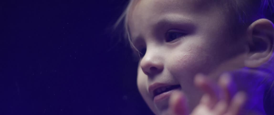 A little girl touches the glass barrier and blows kisses at her dad on the other side