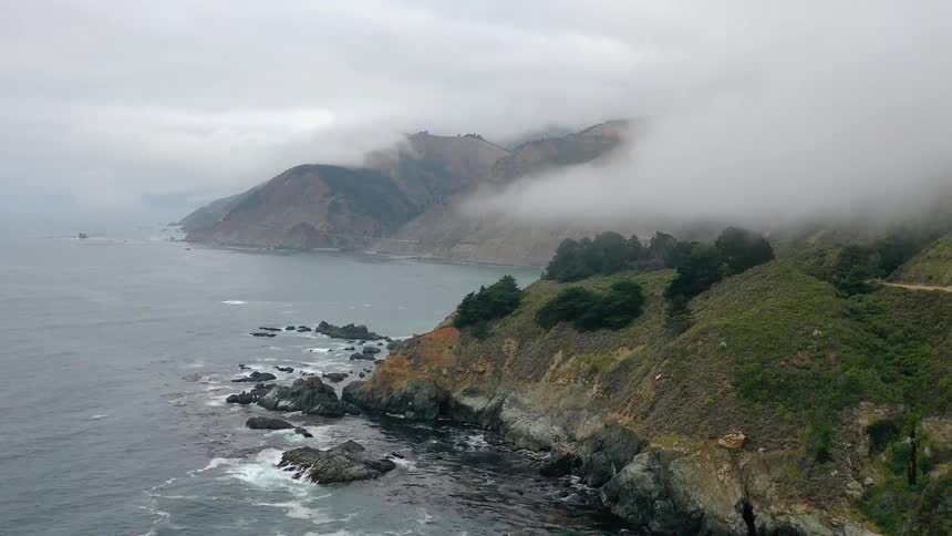 Fog rolls over a mountain that is next to an ocean