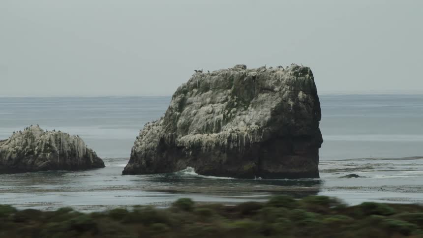 Ocean waves swirl past islets standing just off shore