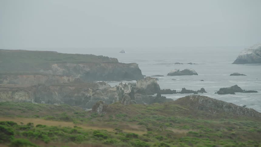 Waves crash onto a rocky shore in the fog