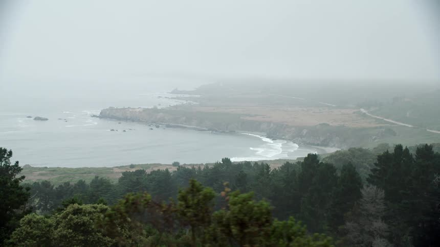 Waves roll in off the ocean under a foggy sky