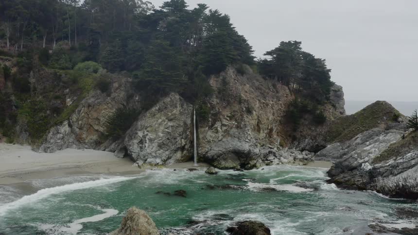 A rocky coast with sand trees and a waterfall