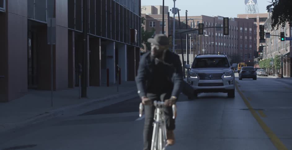 A man is riding his bike down a city street as a vehicle follows