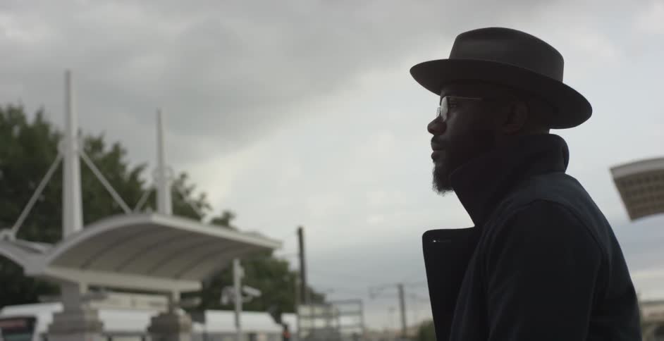 A man is standing on the street as a train passes ahead