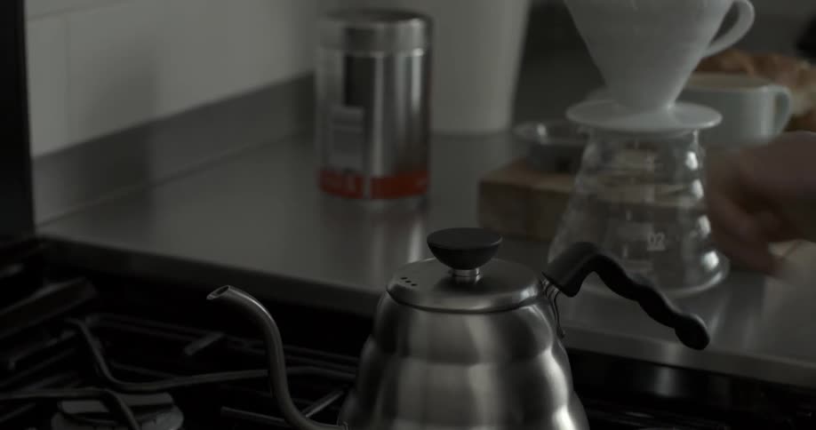 A person puts a coffee pot on a stove