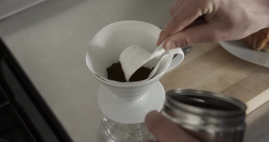 A person spoons coffee into a filer