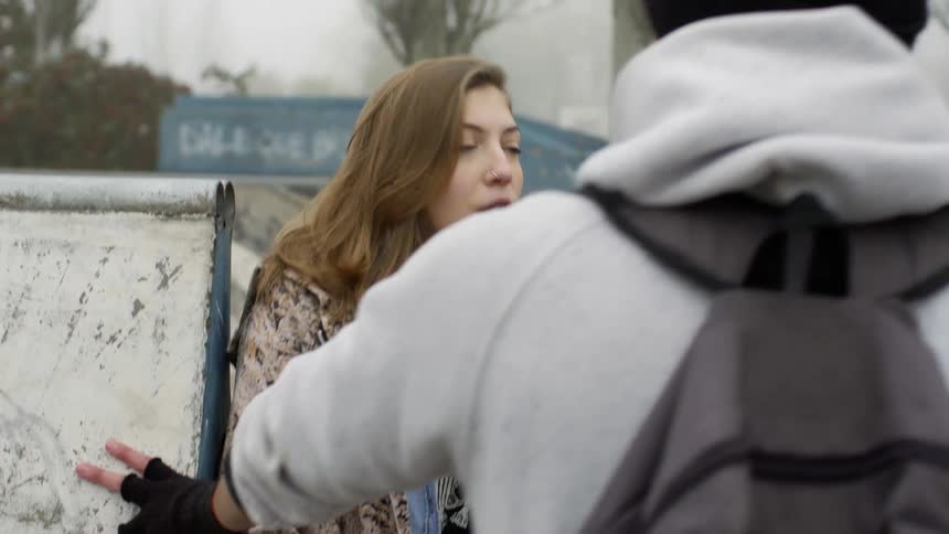 A woman yells at a man as another man watches while they stand next to a graffiti wall