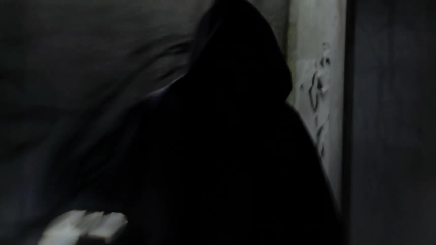 Someone in a black hooded jacket stands in front of a wall