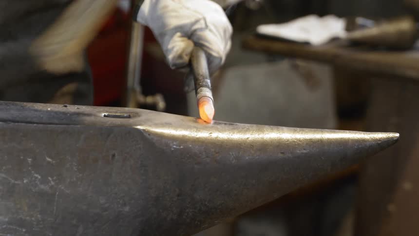 A blacksmith hammers a piece of hot metal with a mallet