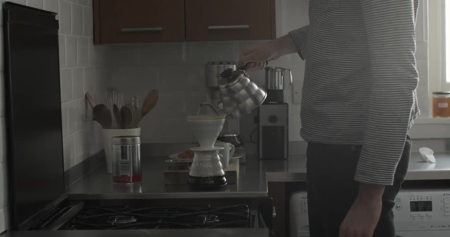 A man lifts a kettle and pours hot water into the filter