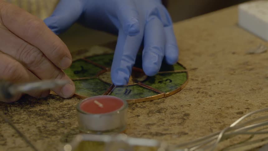 A person arranges pieces of framed glass in a circle preparing for soldering