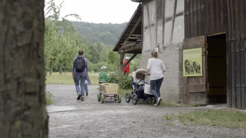 Family follows man around corner of building with forest on the horizon