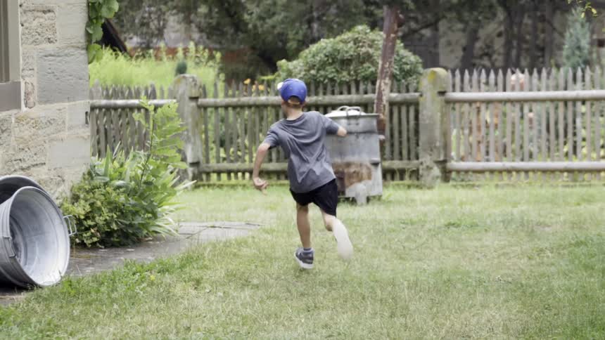 Boy running across the yard and around the corner of a house