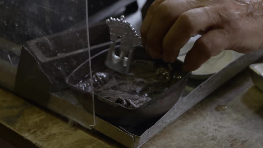 Person picks silver piece up out of solution of clear liquid