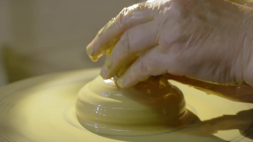 A person shaping clay on a spin wheel