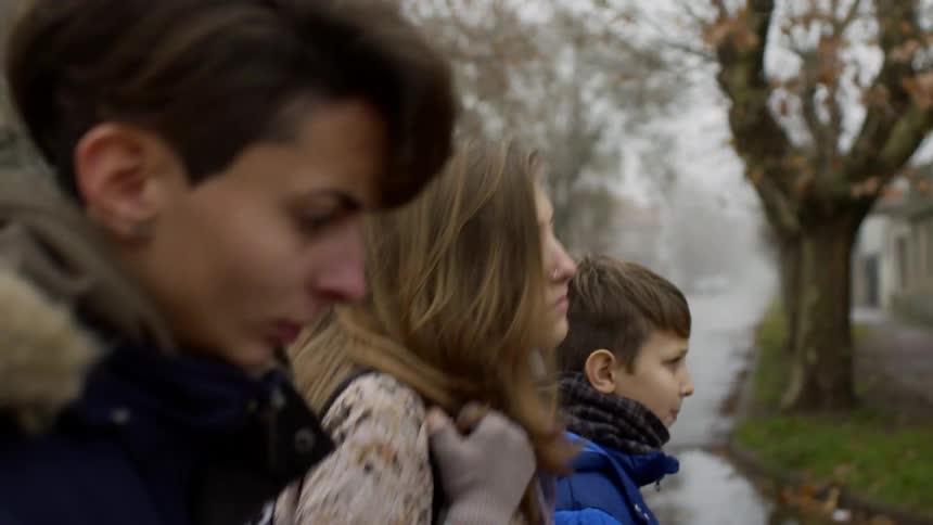 Two teens and a boy walking silently through a neighborhood during the day