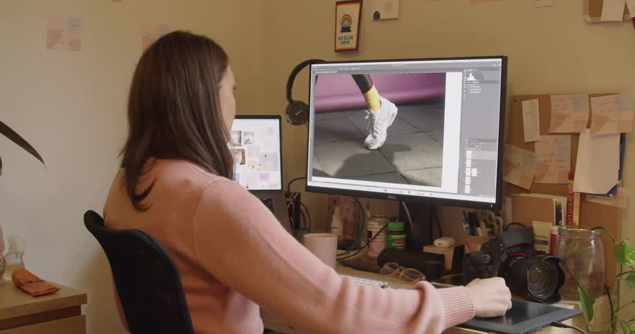 A woman is sitting at a desk working on editing a digital image on her laptop