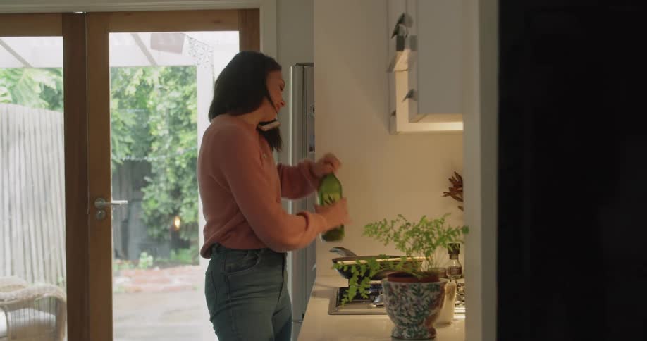 Woman smiles while talking on the mobile phone and drizzling liquid from bottle into dish