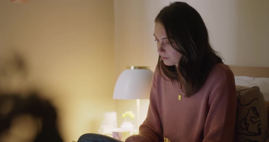 A woman is sitting on her bed typing on her laptop