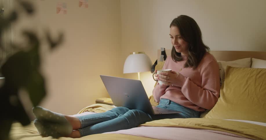 Woman sitting on the bed makes a video call from her laptop in bedroom